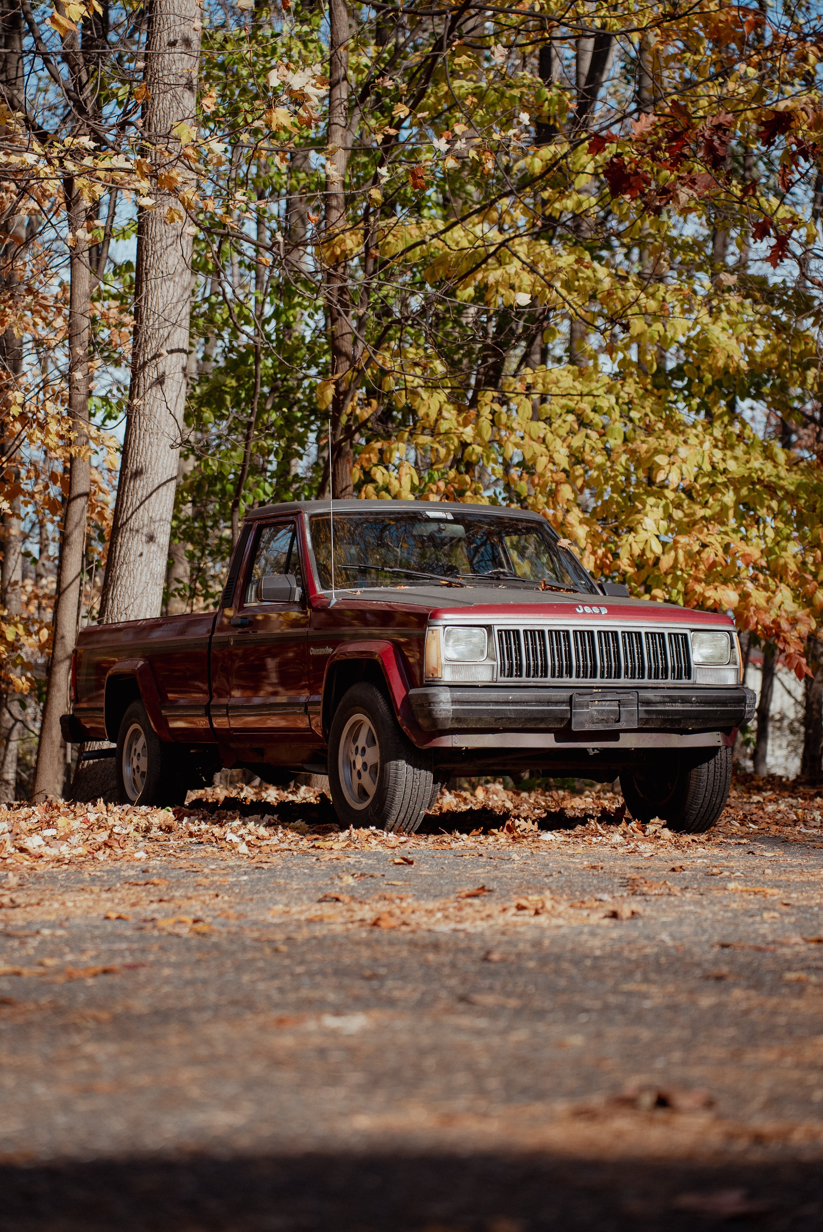 Vintage Comanche truck parked on a dirt road surrounded by trees with autumn foliage
