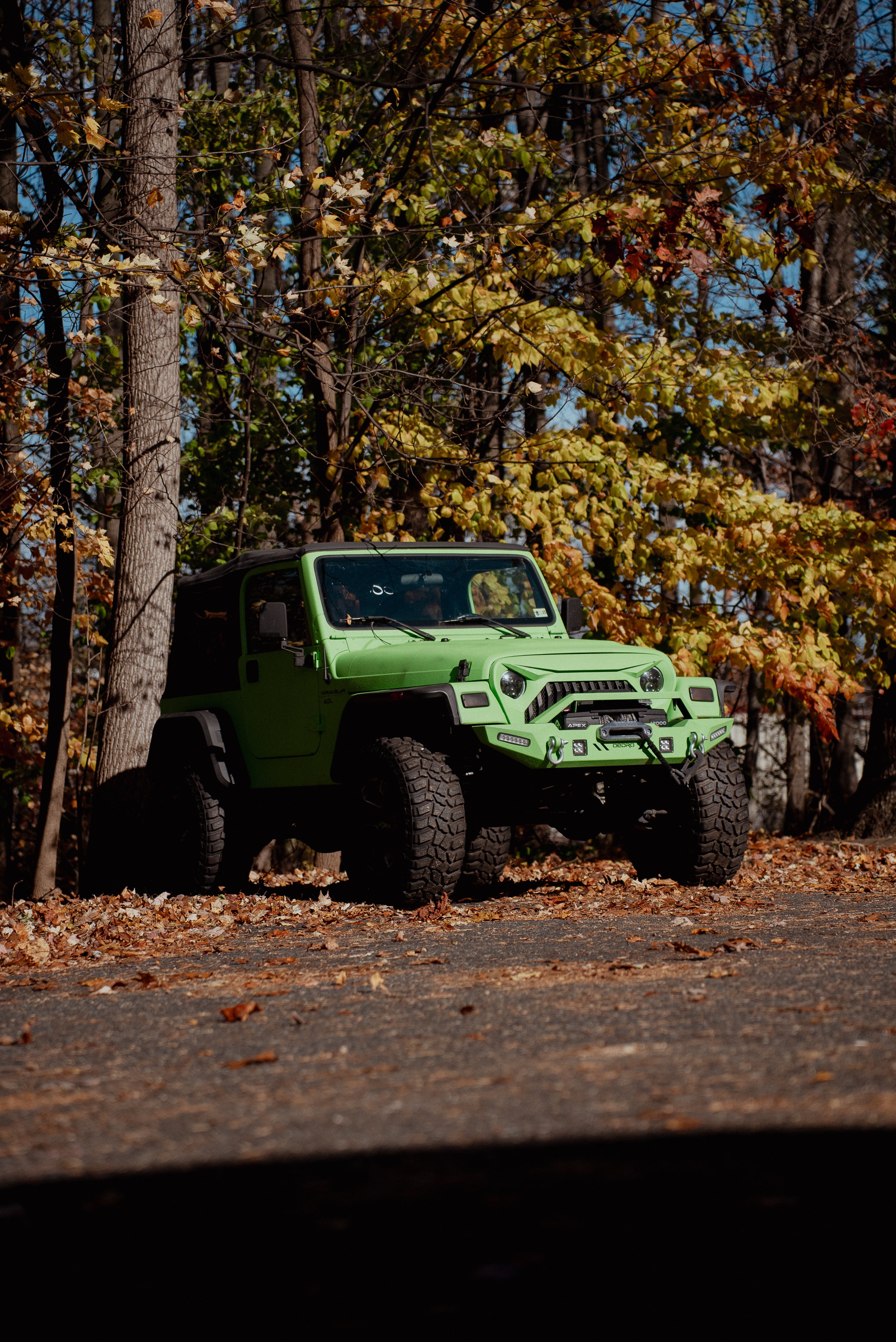 Green off-road vehicle on a dirt road with autumn trees in the background