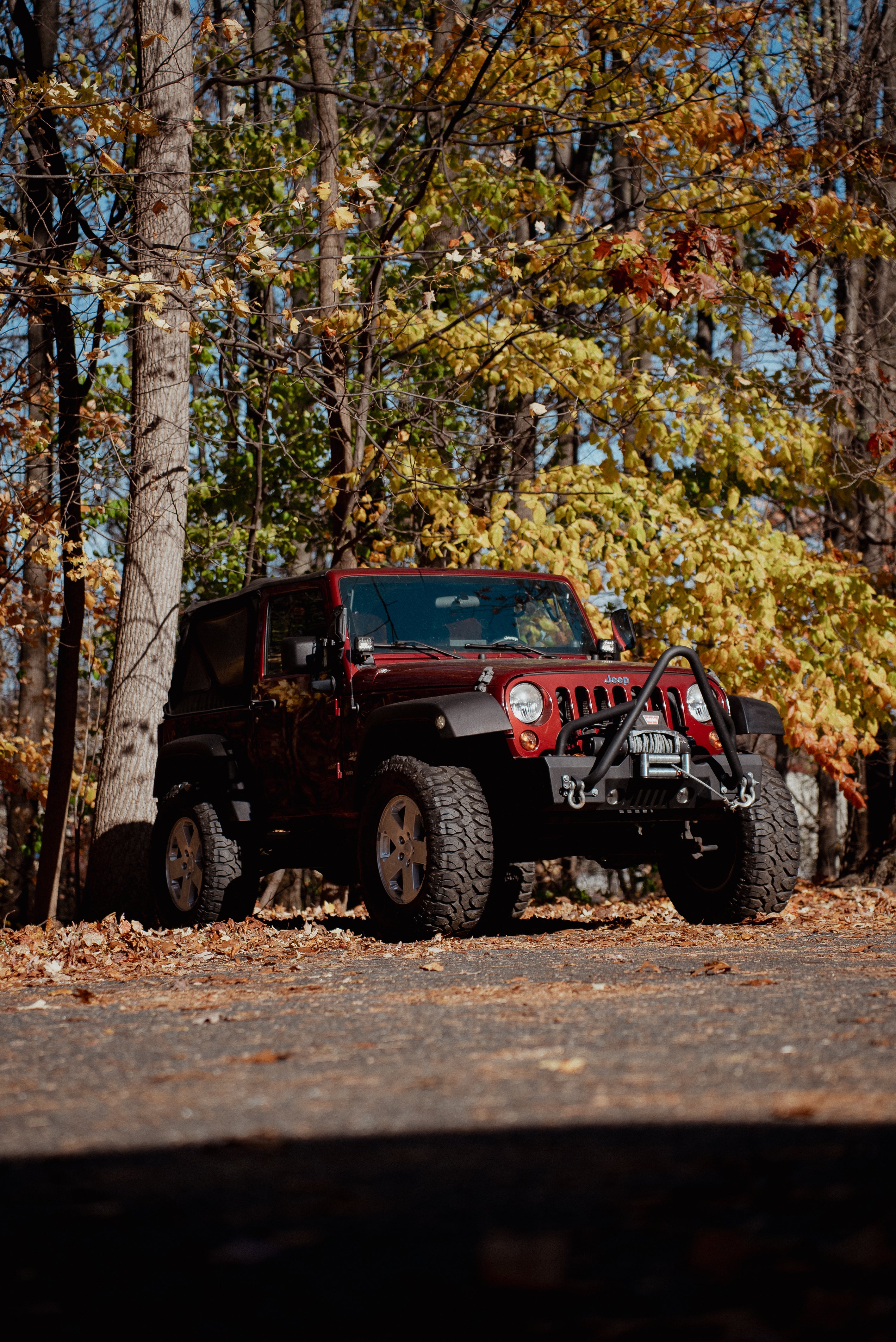 Red Jeep Wrangler parked on a road surrounded by trees with autumn foliage